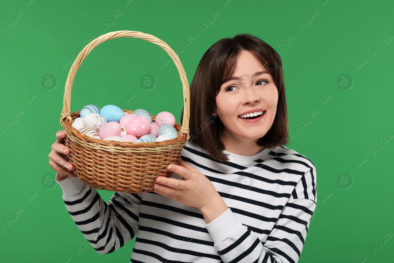 Photo of Easter celebration. Happy woman with wicker basket full of painted eggs on green background