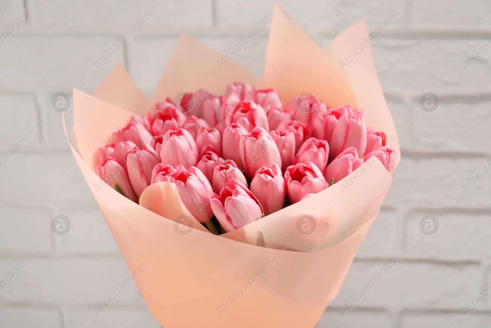 Photo of Bouquet of beautiful pink tulips near white brick wall, closeup