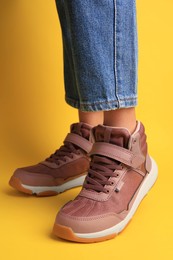 Photo of Girl wearing stylish sneakers on yellow background, closeup