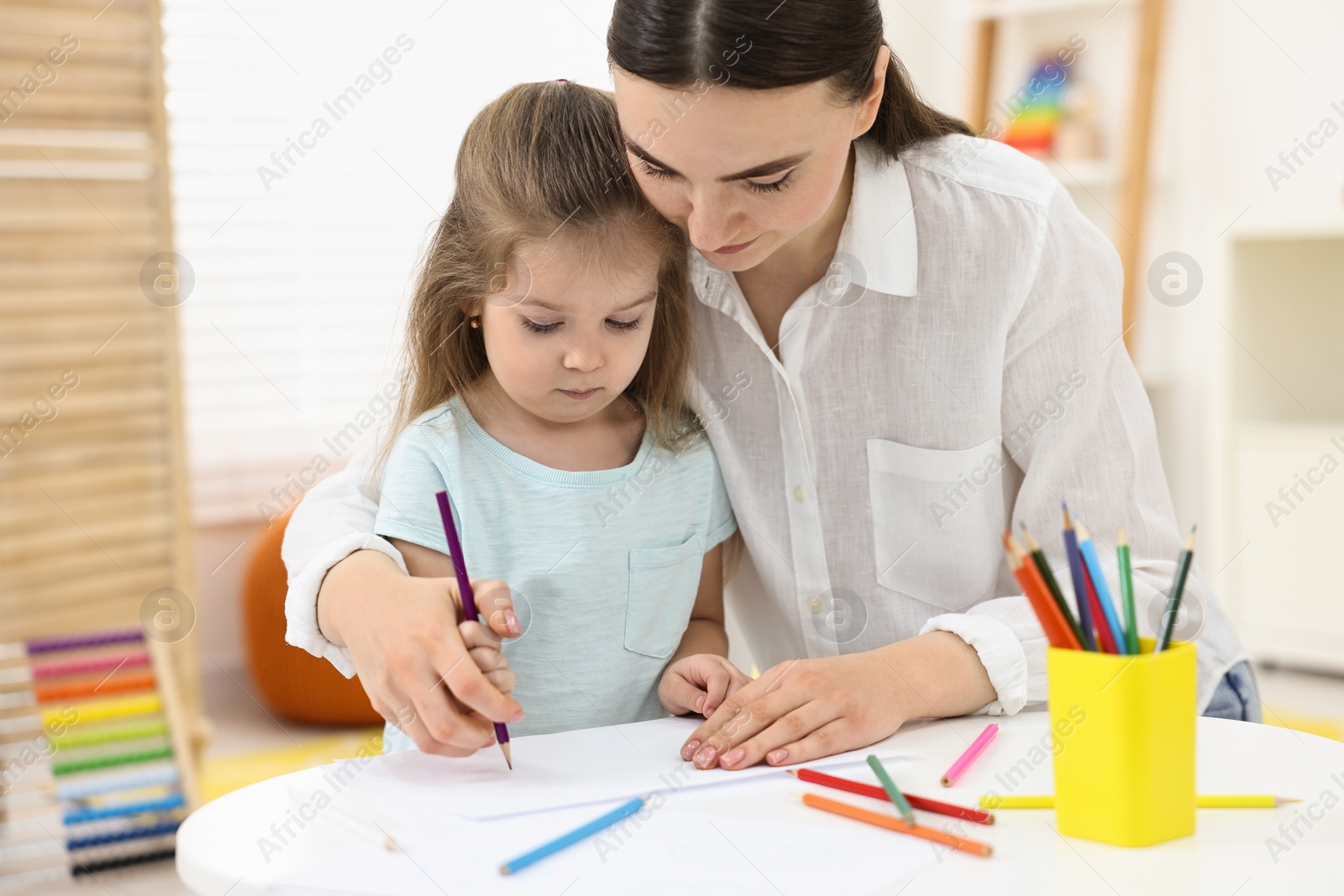 Photo of Mother and her little daughter drawing with colorful pencils at home