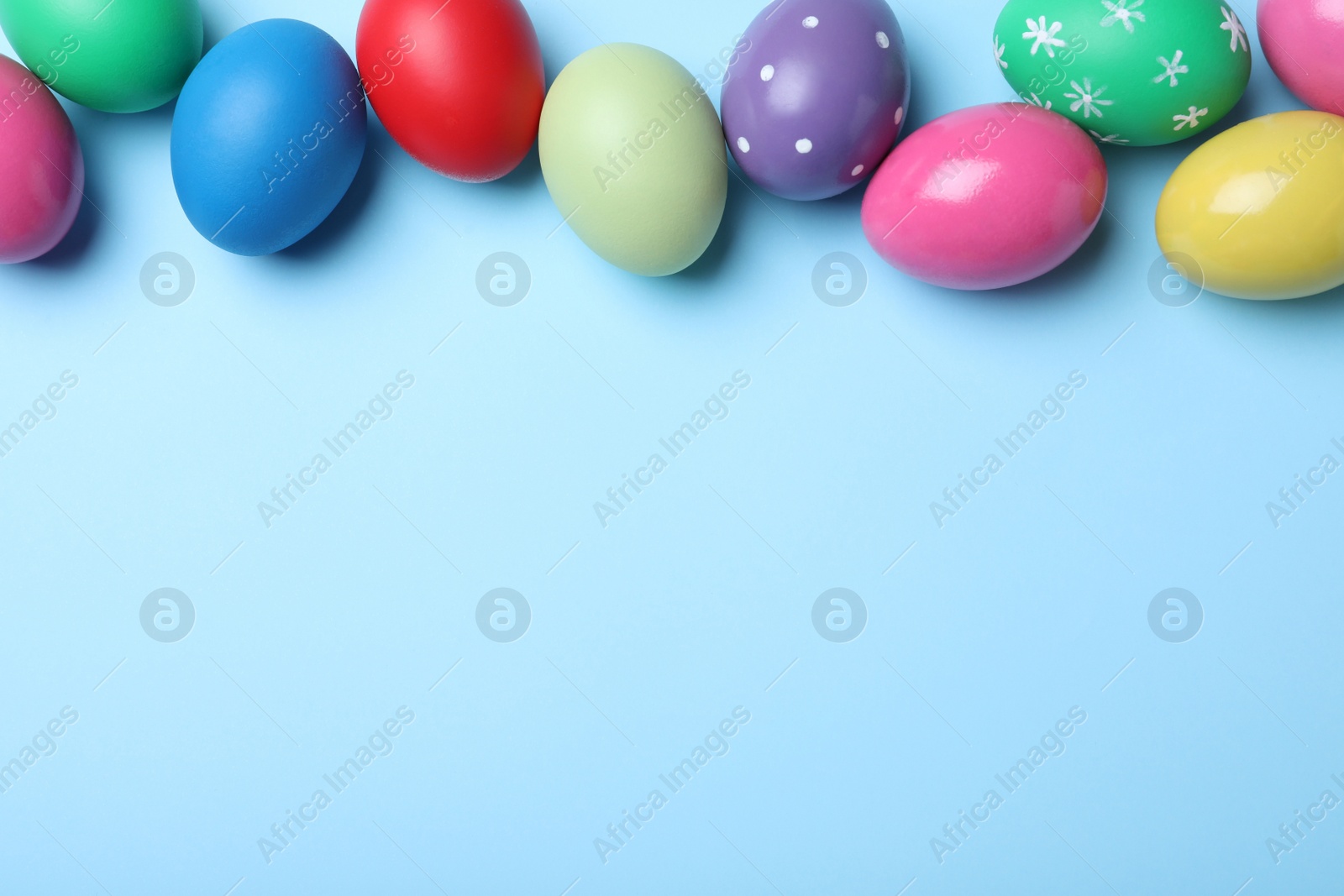 Photo of Bright painted eggs on light blue background, flat lay with space for text. Happy Easter