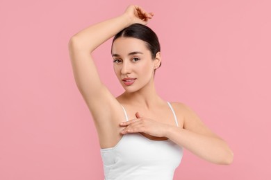 Beautiful woman showing armpit with smooth clean skin on pink background