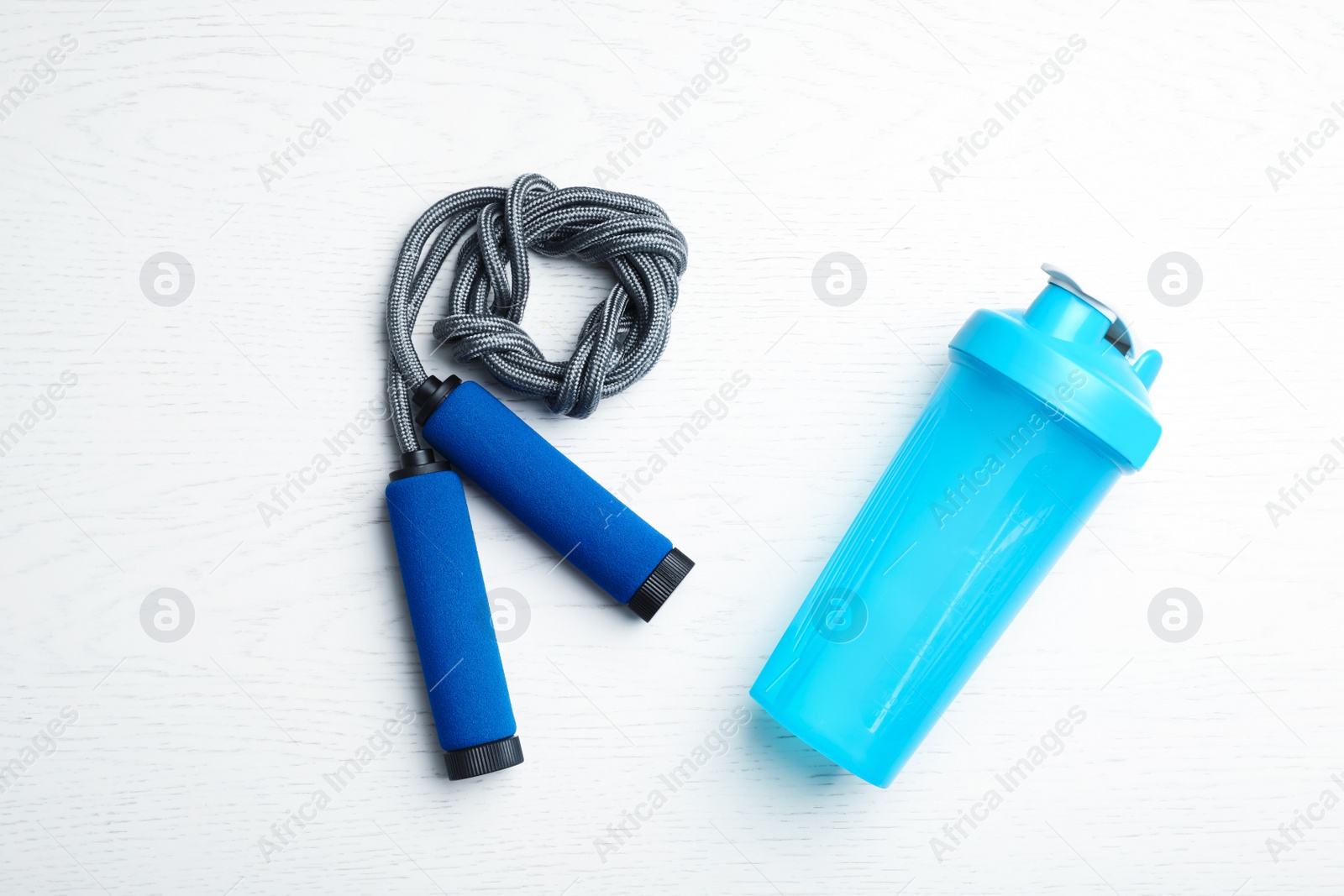 Photo of Jump rope and bottle of water on white wooden background, top view