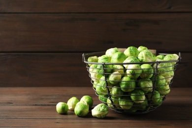 Photo of Metal basket with fresh Brussels sprouts on table against wooden background. Space for text