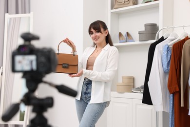 Photo of Smiling fashion blogger showing her bag while recording video at home