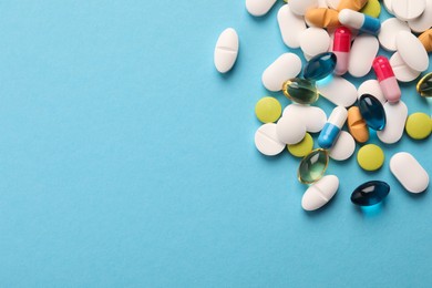 Photo of Pile of different pills on light blue background, flat lay. Space for text