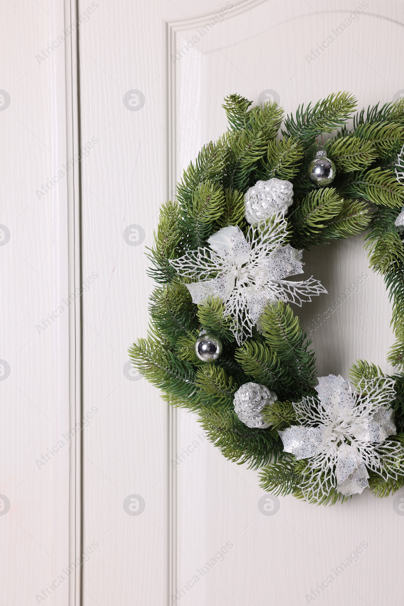 Photo of Beautiful Christmas wreath with festive decor hanging on white door