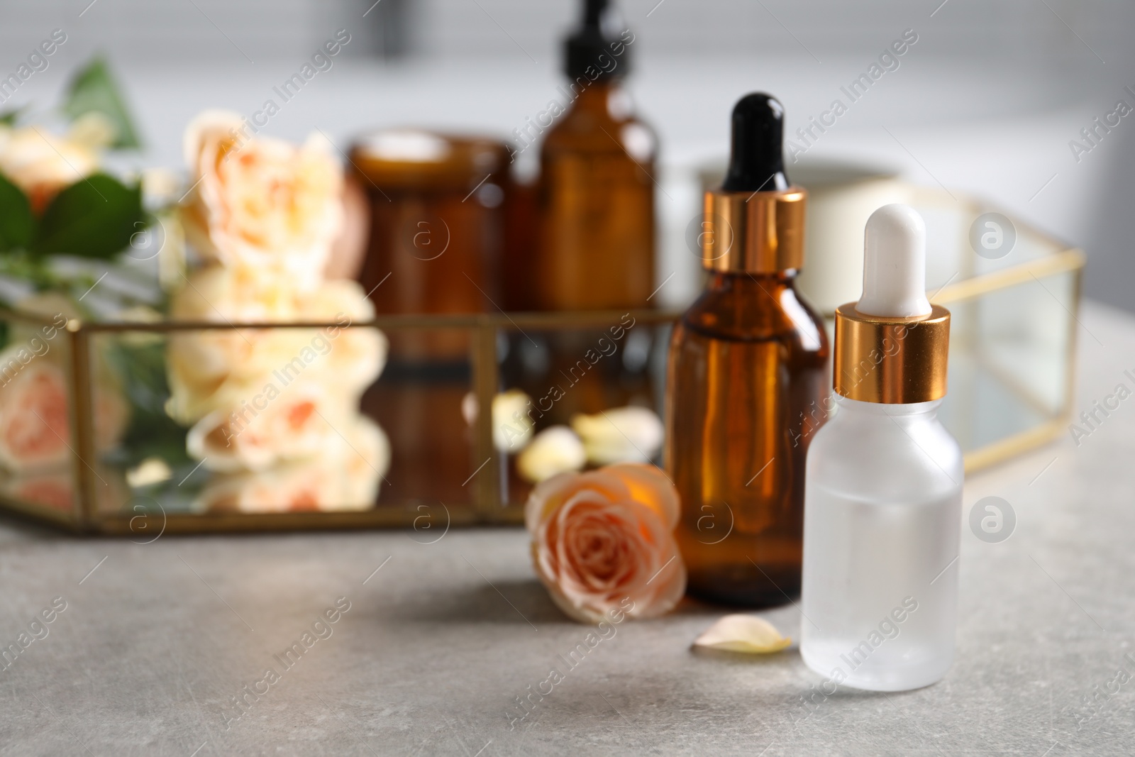Photo of Bottles of cosmetic serum and beautiful flower on gray table, closeup