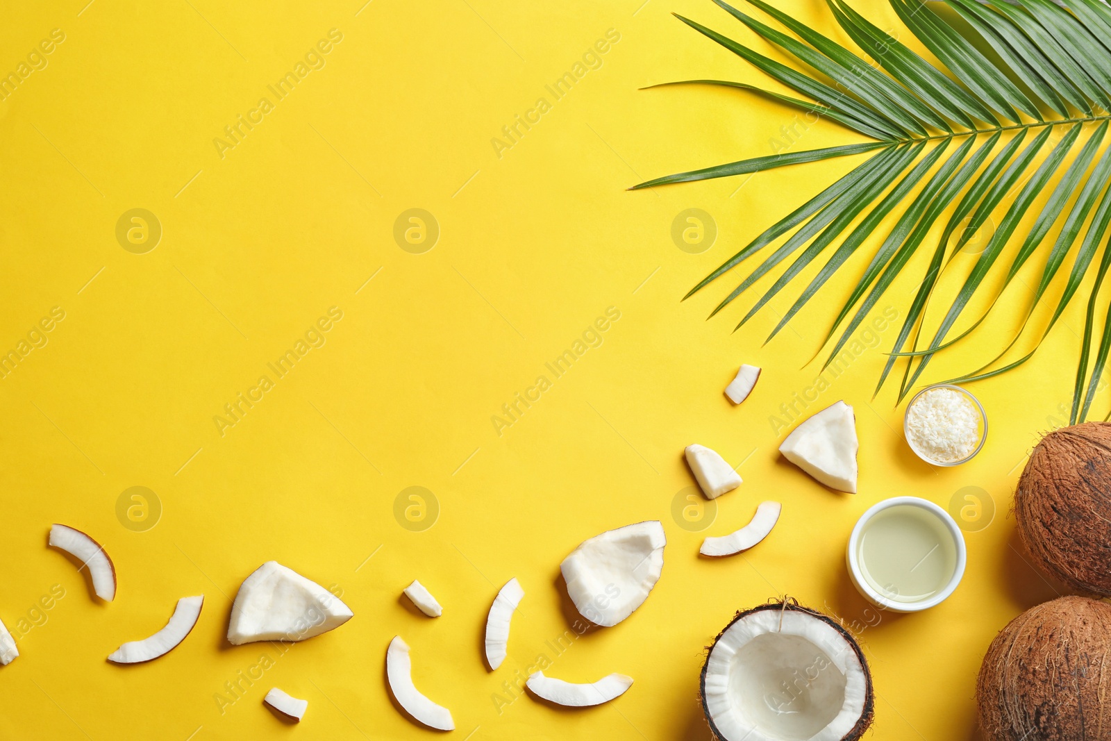 Photo of Bowl of natural organic oil and coconuts on yellow background, flat lay. Space for text