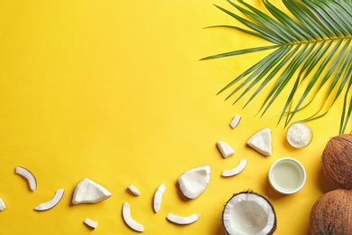 Photo of Bowl of natural organic oil and coconuts on yellow background, flat lay. Space for text