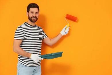 Photo of Designer painting orange wall with roller. Space for text