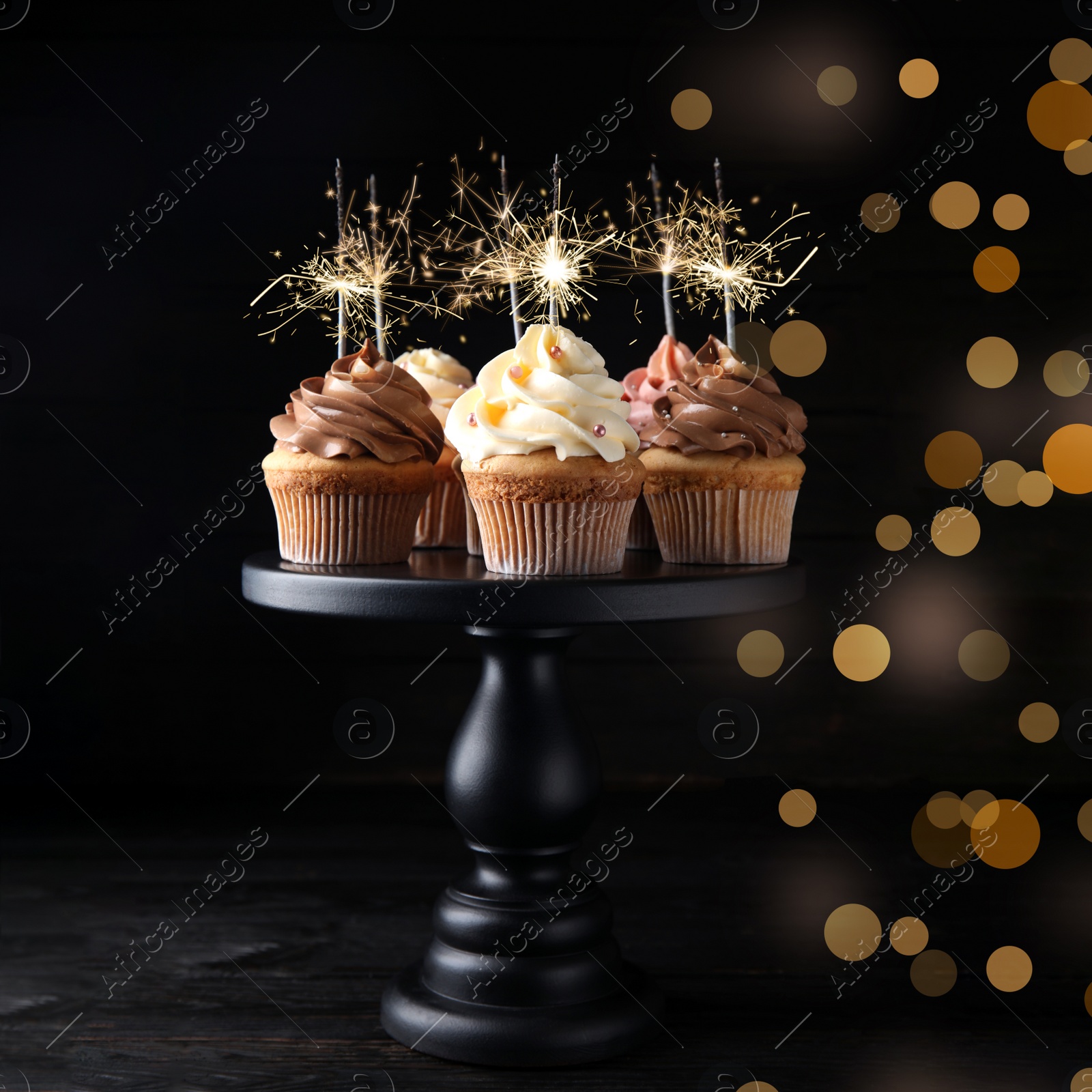 Image of Birthday cupcakes with sparklers on wooden table against dark background