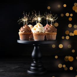 Image of Birthday cupcakes with sparklers on wooden table against dark background