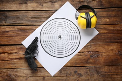 Photo of Shooting target, handgun and headphones on wooden table, top view