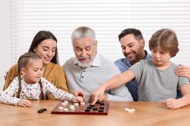 Photo of Playing checkers. Parents and grandfather looking at children's game in room