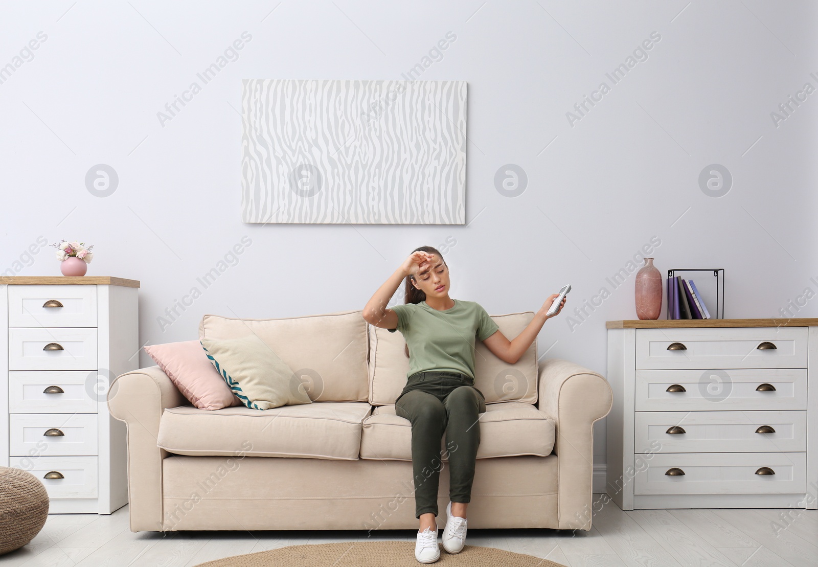 Photo of Young woman switching on air conditioner with remote control at home