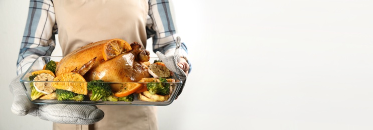Photo of Woman holding pan with chicken, oranges and vegetables on light background, closeup