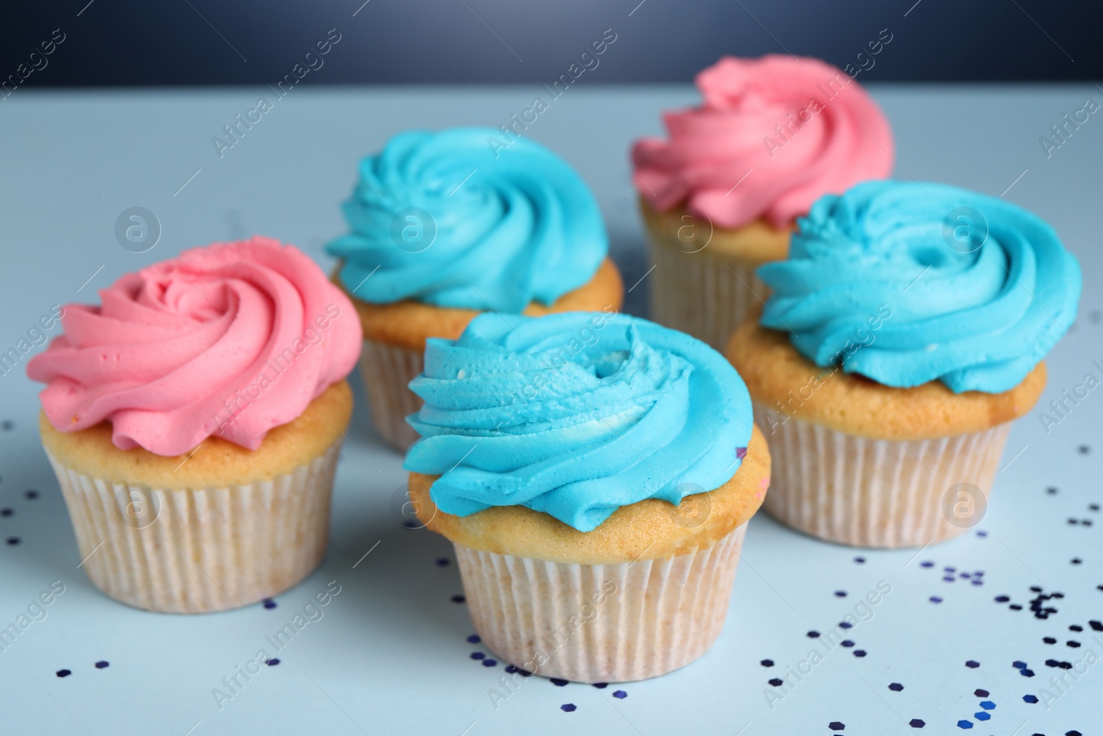 Photo of Delicious cupcakes with bright cream and confetti on blue background, closeup