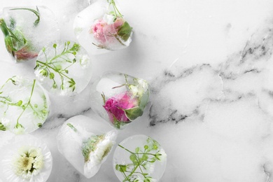 Photo of Ice cubes with flowers on marble background, flat lay. Space for text