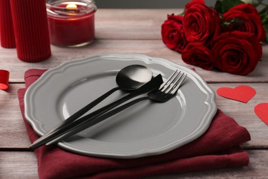 Photo of Romantic place setting with red roses and candle on wooden table. St. Valentine's day dinner
