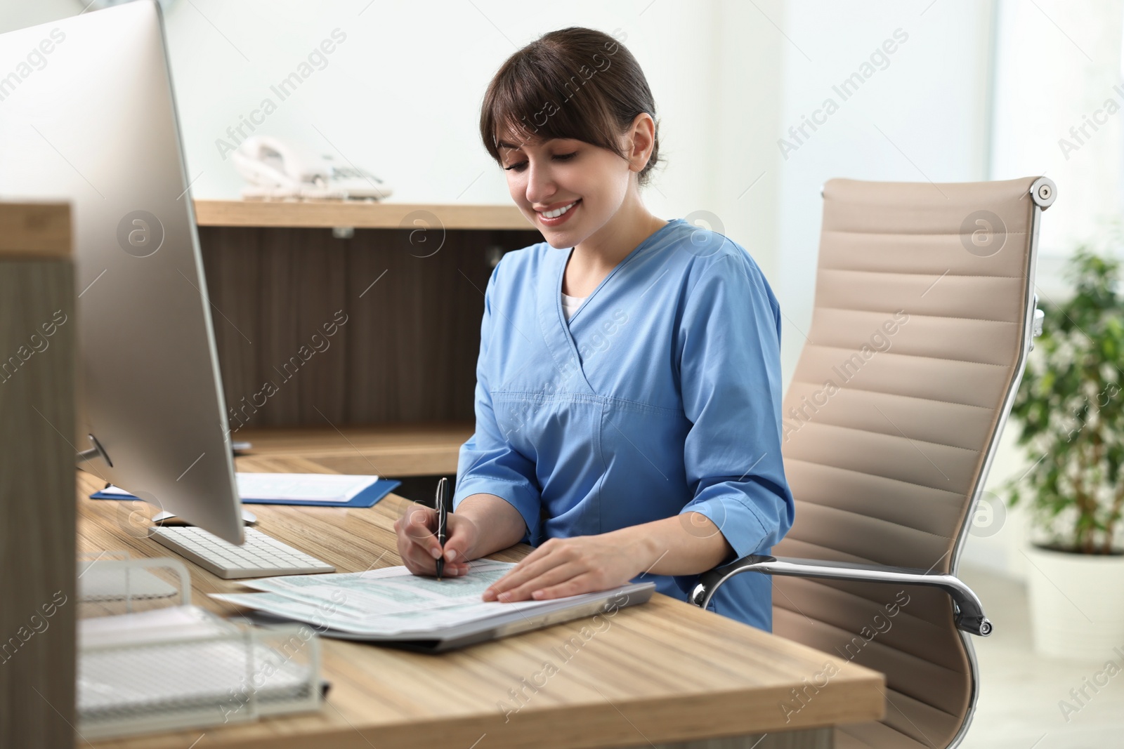 Photo of Smiling medical assistant working with documents in office