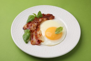 Fried egg, bacon and basil on green background