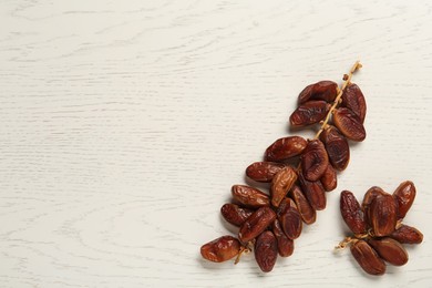 Photo of Branches of tasty sweet dried dates on white wooden table, flat lay. Space for text