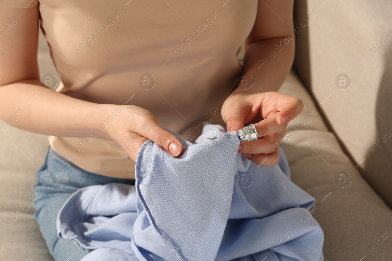 Photo of Woman sewing on light blue with thimble and needle indoors, closeup