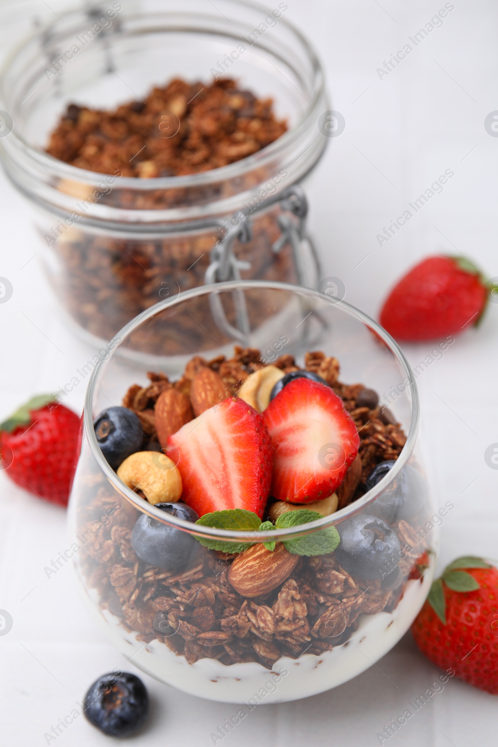 Photo of Tasty granola with berries, nuts and yogurt in glass on white table, closeup