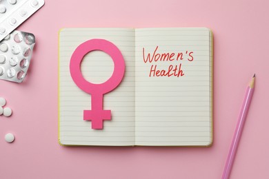 Photo of Notebook with female gender sign, pills and text Women's Health on pink background, flat lay
