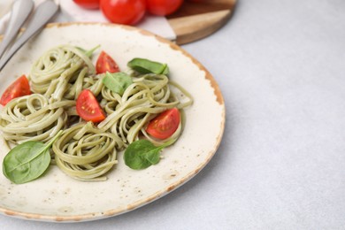 Photo of Tasty pasta with spinach and tomatoes on light grey table, closeup. Space for text