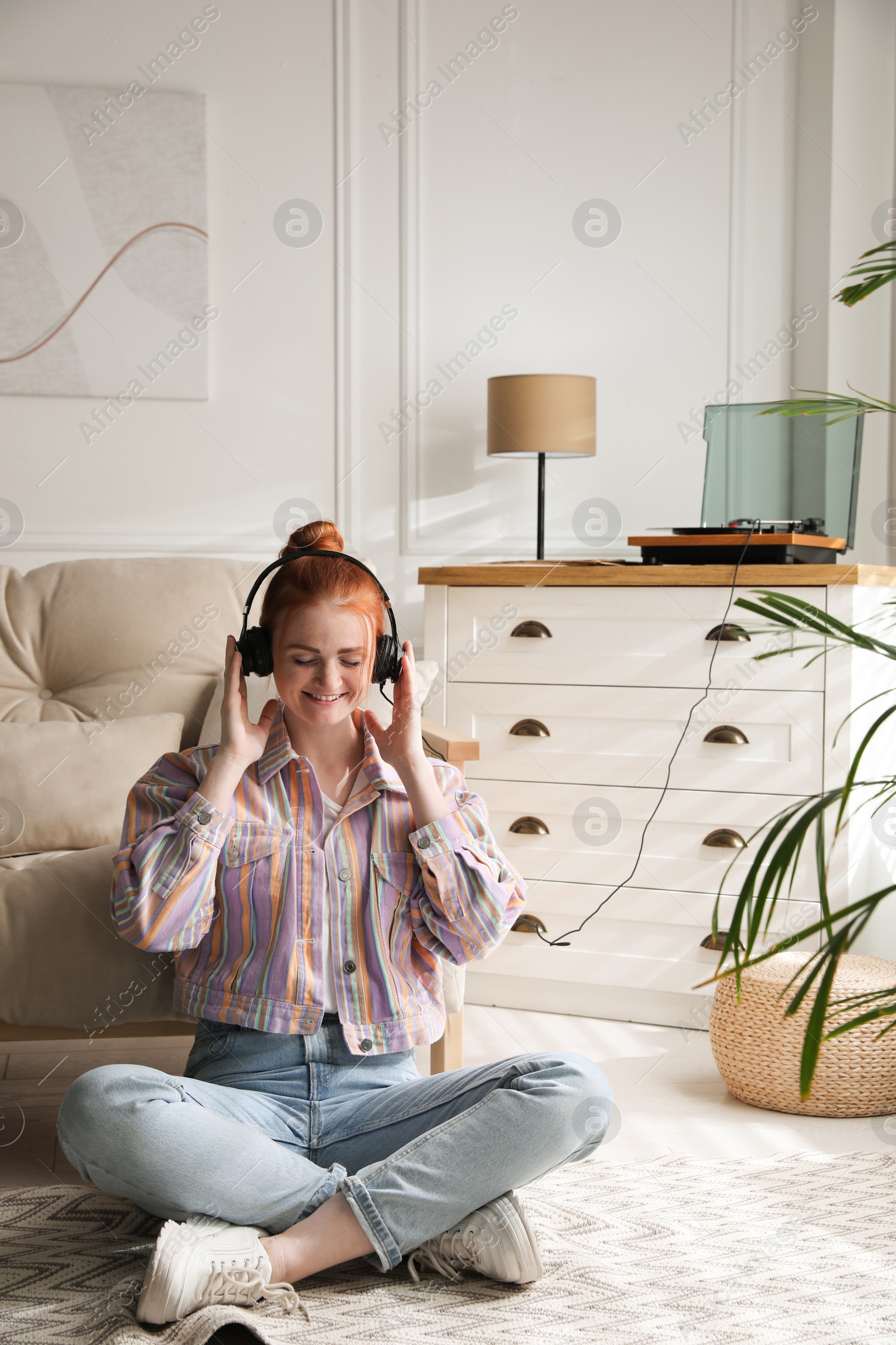 Photo of Young woman listening to music with turntable in living room