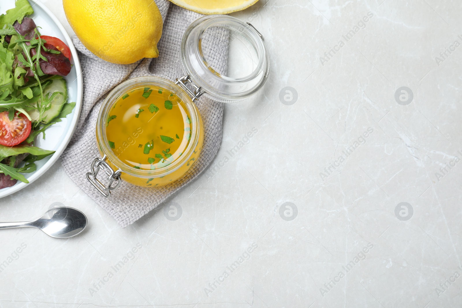 Photo of Jar of lemon dressing near salad on light table, flat lay with space for text