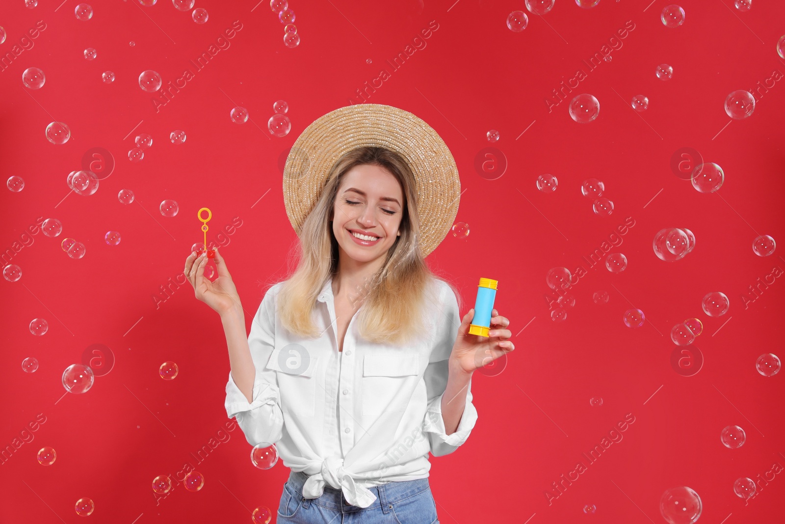 Photo of Young woman blowing soap bubbles on red background, space for text