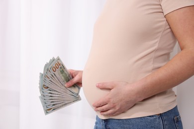 Surrogate mother. Pregnant woman with dollar banknotes indoors, closeup