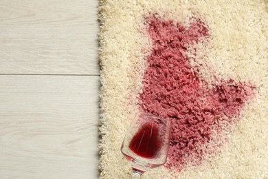 Photo of Overturned glass and spilled red wine on beige carpet, top view. Space for text