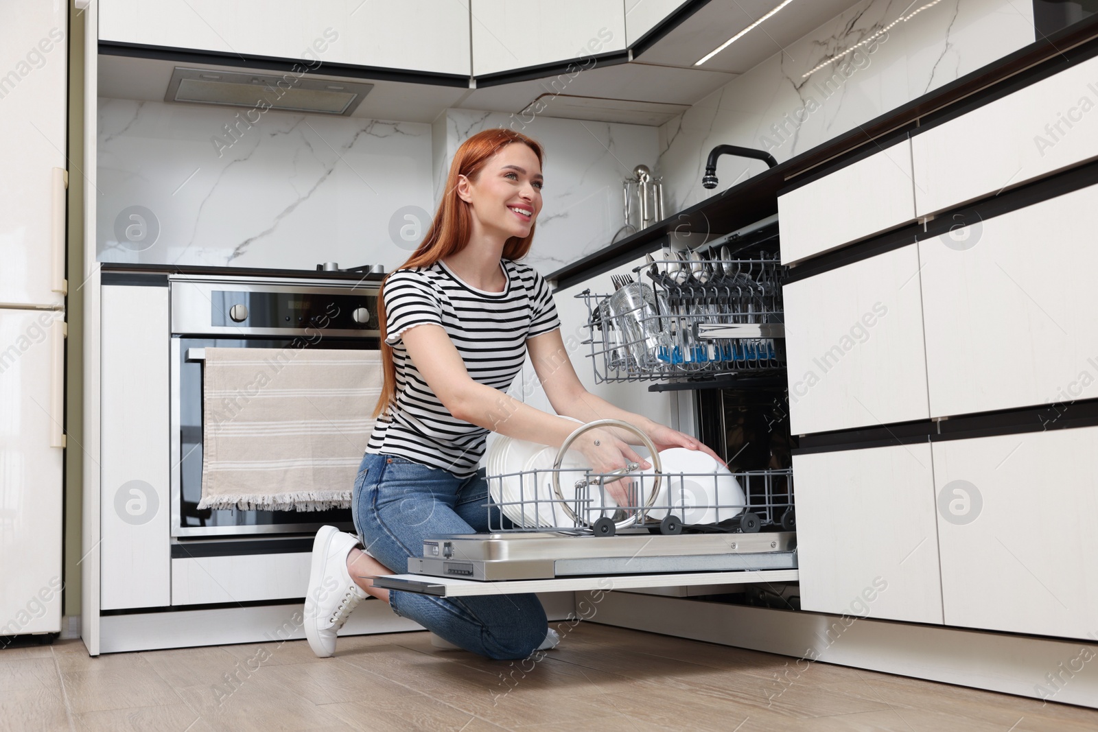 Photo of Smiling woman loading dishwasher with plates in kitchen