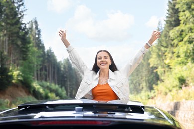 Photo of Enjoying trip. Happy woman leaning out of car roof outdoors