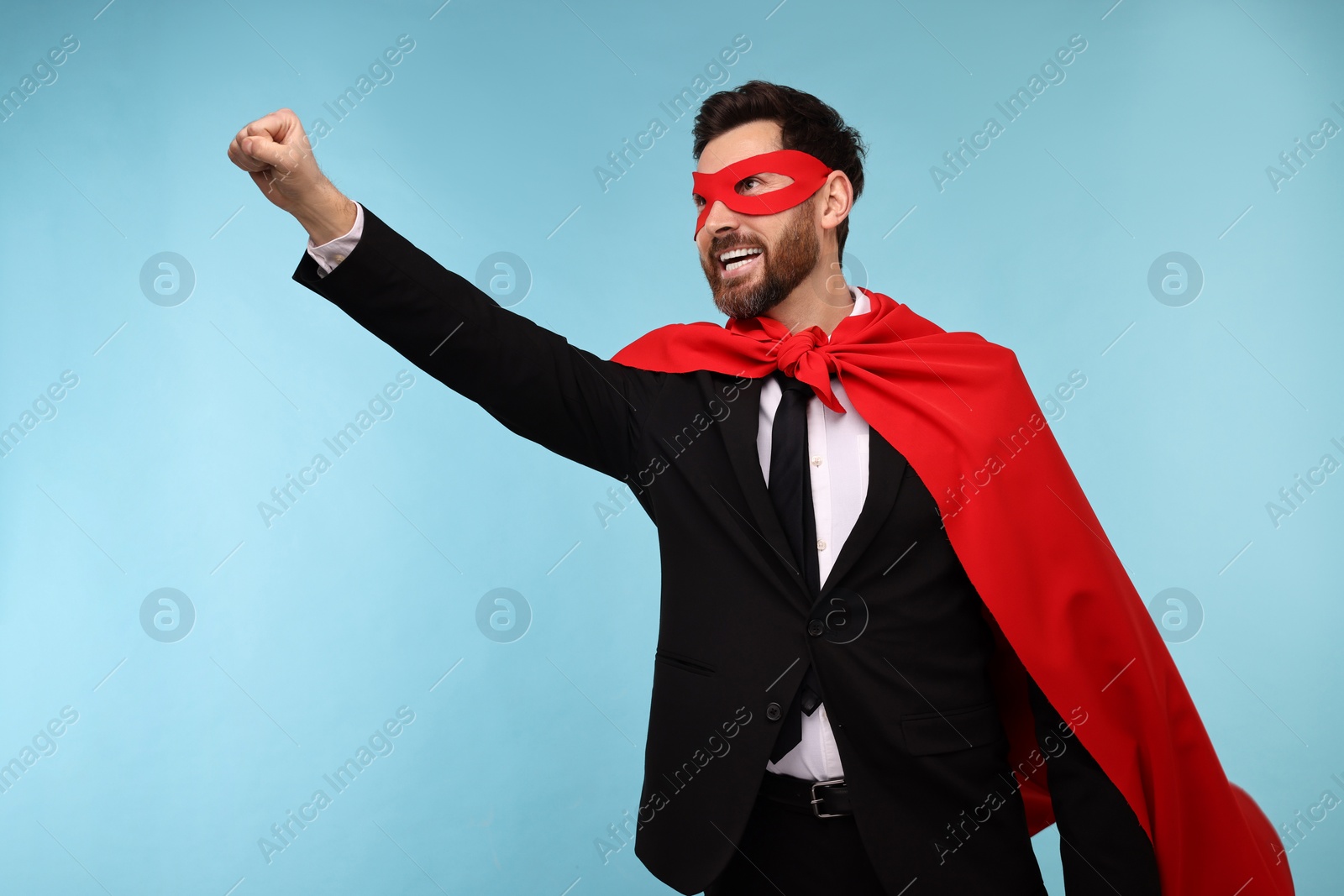 Photo of Businessman wearing red superhero cape and mask on light blue background