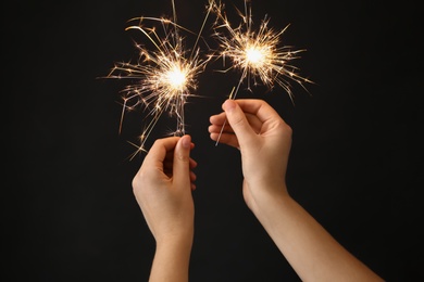 Photo of Woman holding bright burning sparklers on black background, closeup