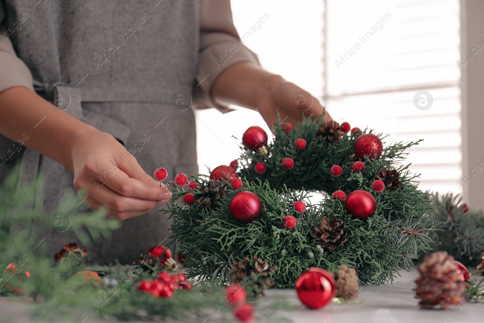 Photo of Florist making beautiful Christmas wreath at grey table indoors, closeup