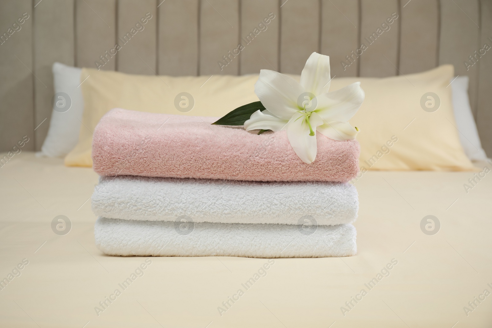 Photo of Stack of clean towels and flower on bed