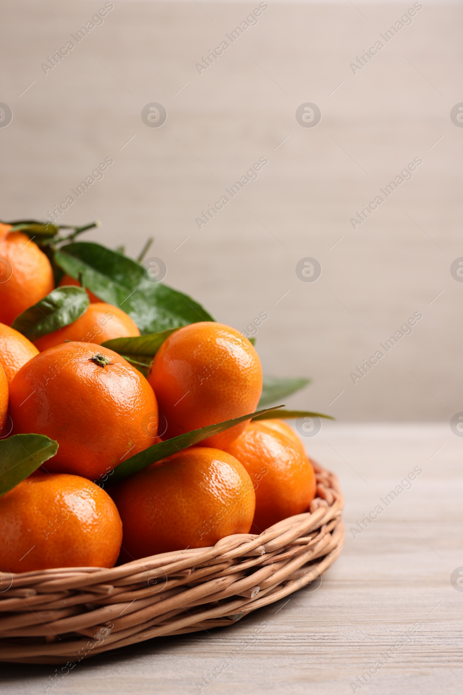 Photo of Fresh ripe juicy tangerines and green leaves on white wooden table, space for text