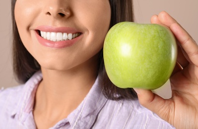 Young woman with healthy teeth and apple on color background, closeup