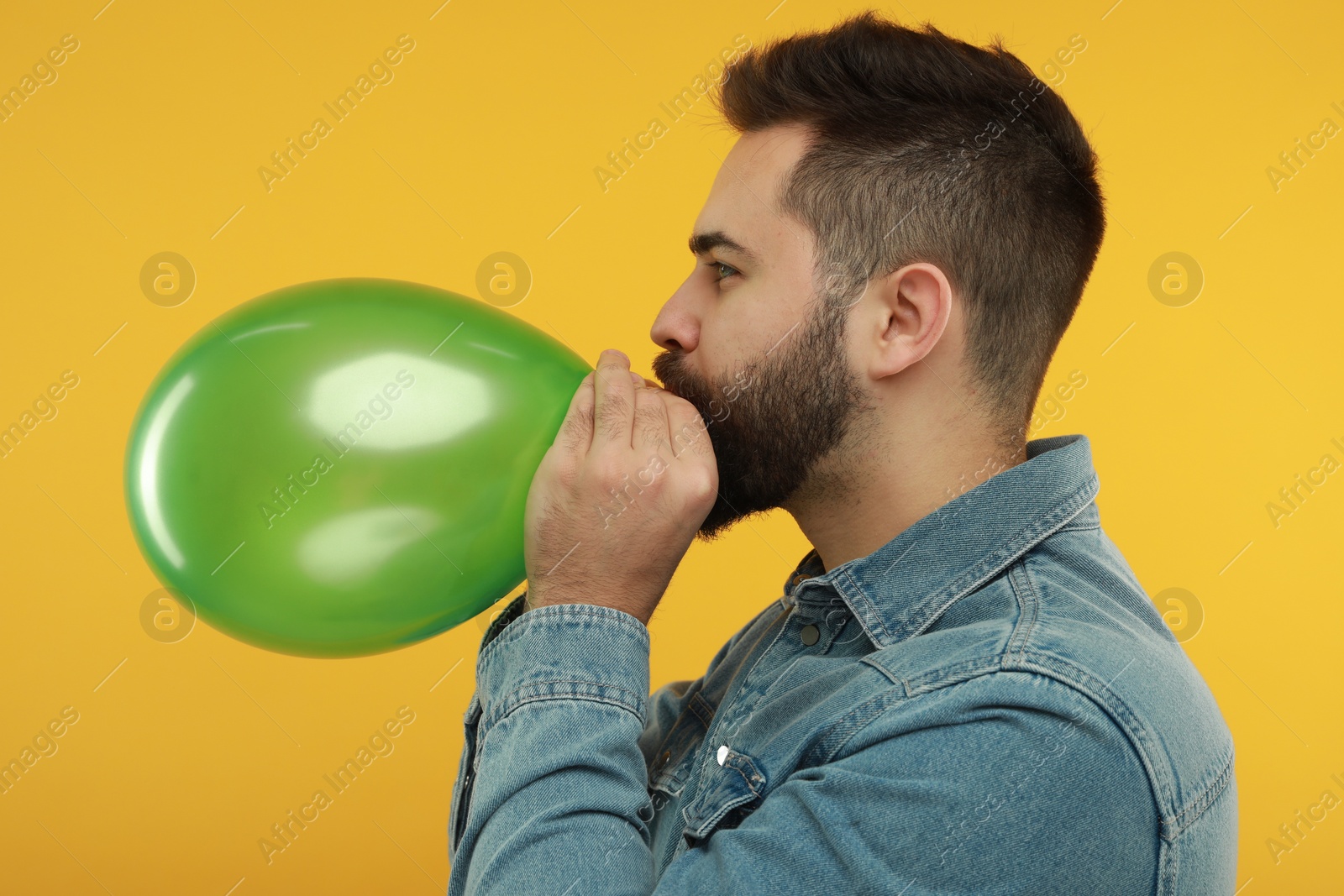 Photo of Man inflating bright balloon on yellow background