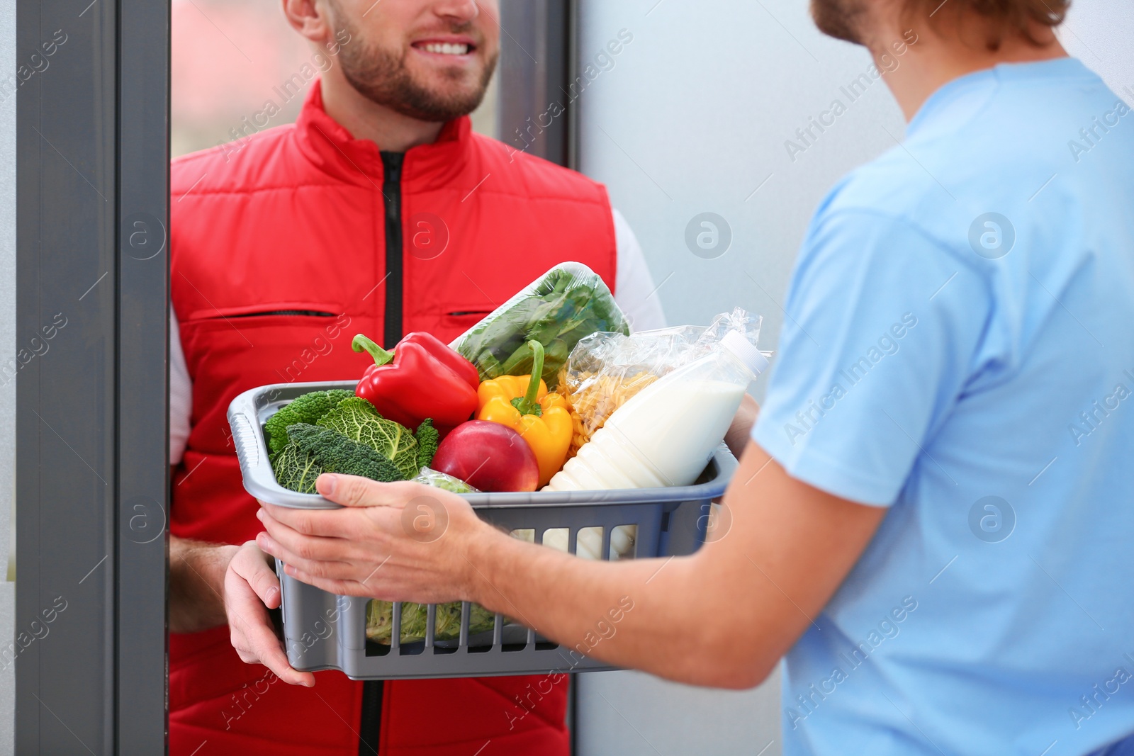 Photo of Courier giving plastic crate with products to customer at home, closeup. Food delivery service