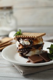 Photo of Delicious marshmallow sandwich with cracker and chocolate on white wooden table, closeup