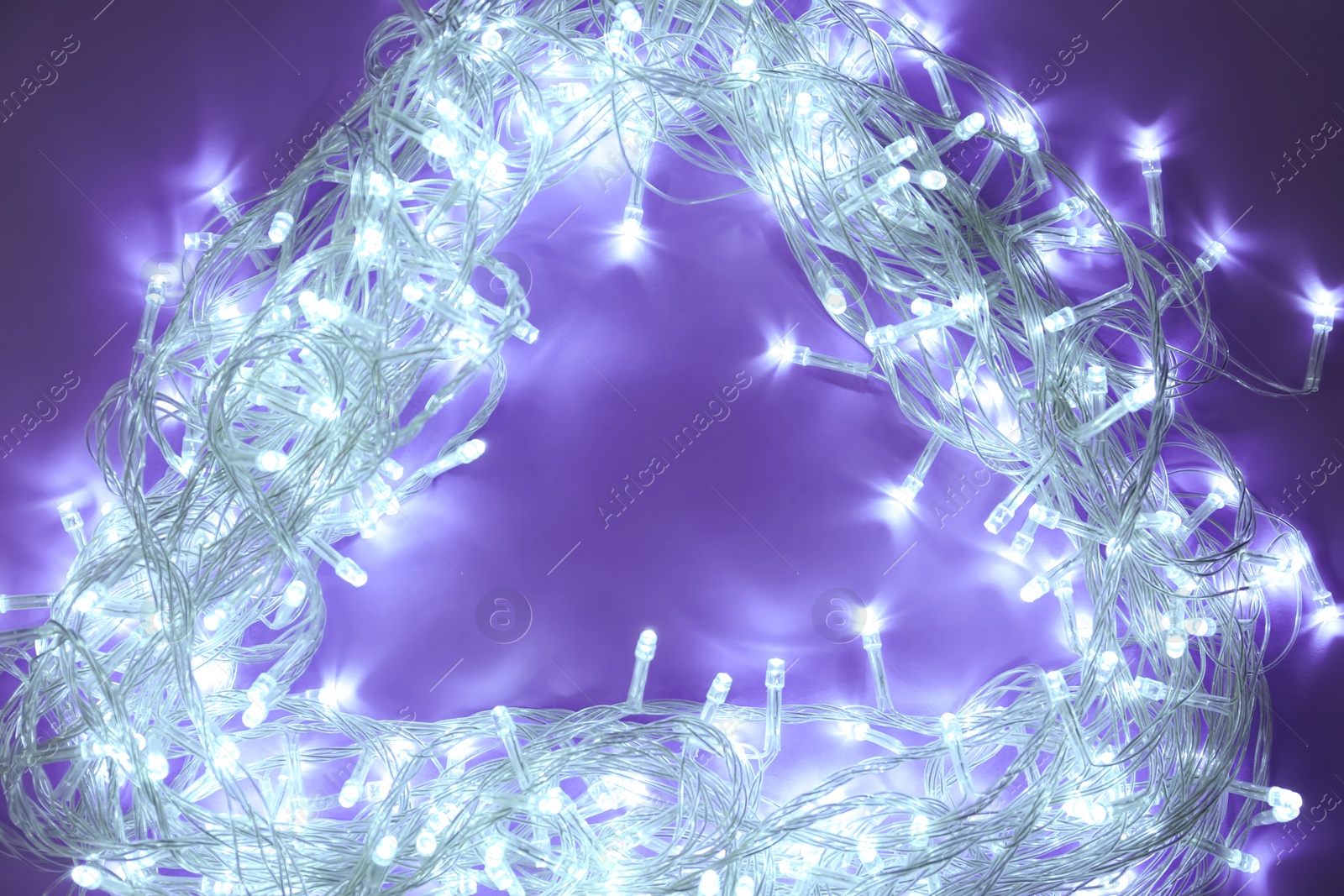 Photo of Frame made of glowing Christmas lights on violet background, top view. Space for text