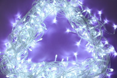 Photo of Frame made of glowing Christmas lights on violet background, top view. Space for text