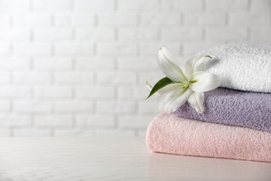 Photo of Stack of clean bath towels and beautiful flower on white wooden table. Space for text